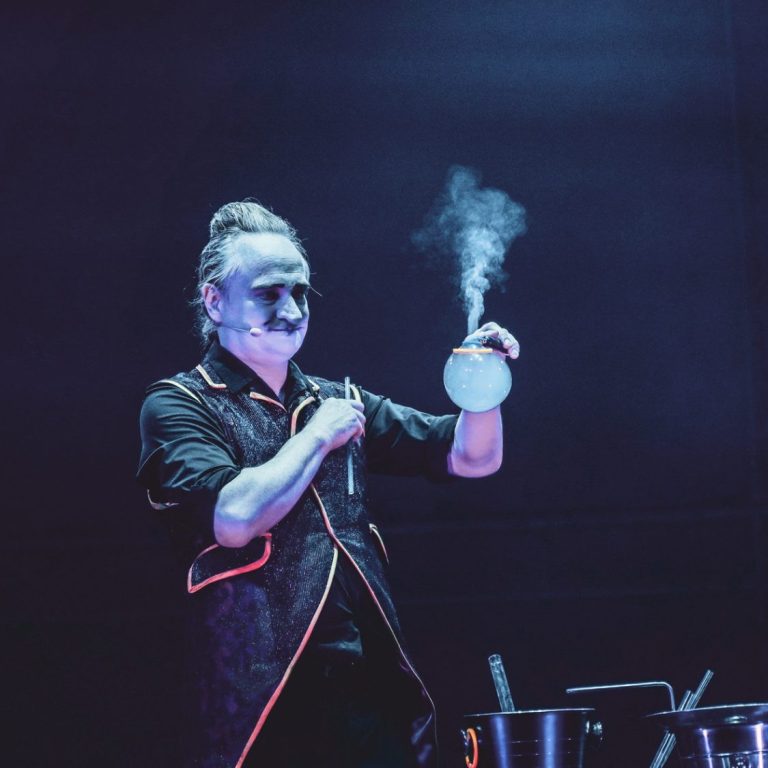 Seifenblasenkünstler Stephan Masur mit Rauchseifenblase Ein Zauberer hält eine schimmernde Seifenblase mit Rauch darüber in einer dunklen Umgebung.