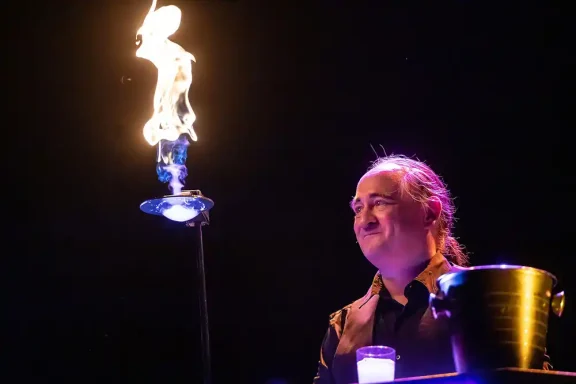 Burning Bubble Stephan Masur Ein Mann lächelt, während eine Flamme über einem Tisch brennt.