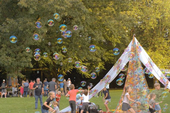 Kinder spielen vor einem bunten Zelt mit Seifenblasen im Park.